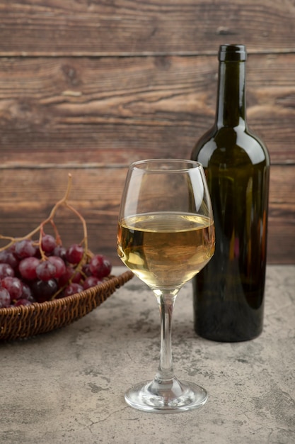 Cesta de mimbre de uvas rojas con copa de vino blanco sobre mesa de mármol.