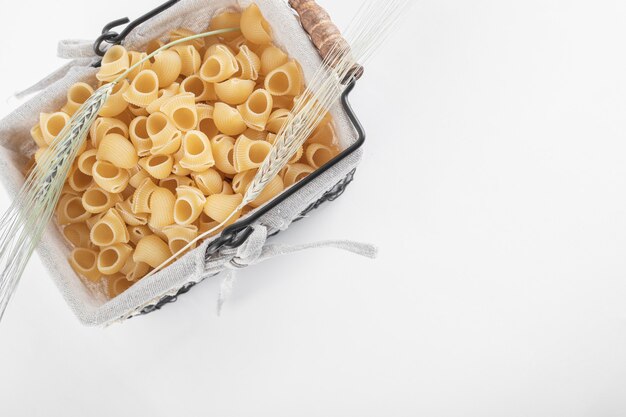 Cesta de pasta cruda con espigas de trigo sobre fondo blanco. Foto de alta calidad