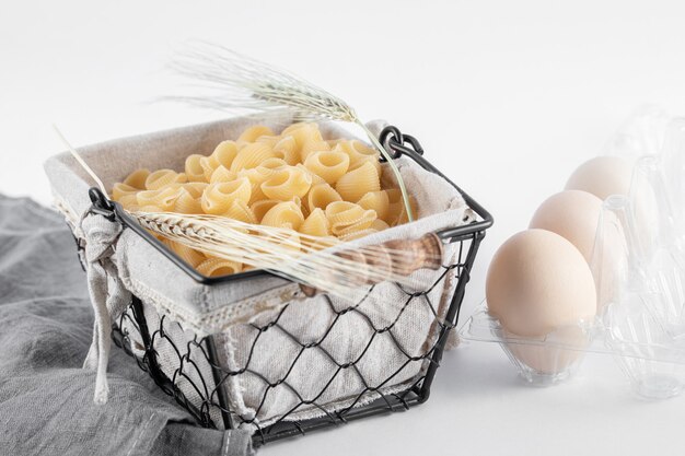 Cesta de pasta cruda y huevos en recipiente sobre superficie blanca.