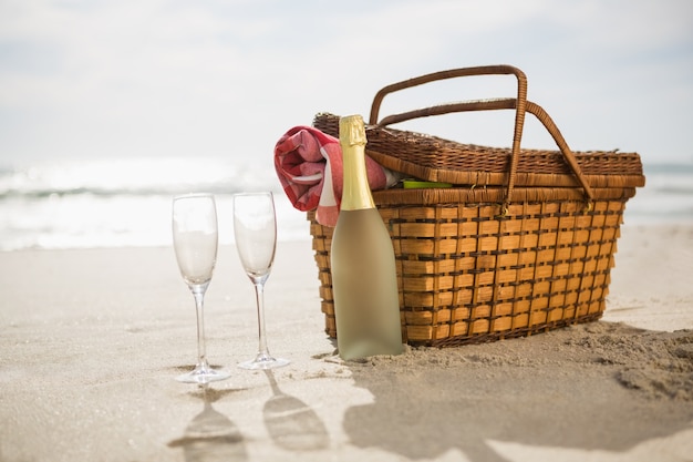 cesta de picnic, botella de champagne y dos copas en la arena