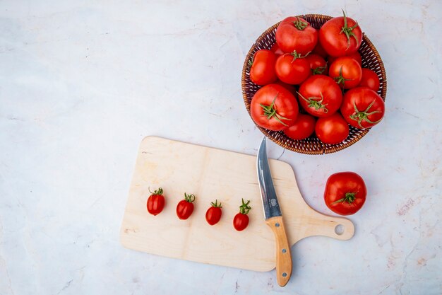 Cesta de tomates y tabla de cortar sobre superficie blanca