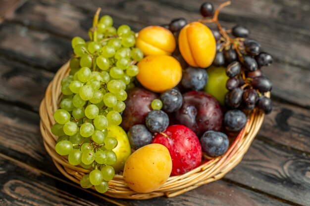 Cesta de vista frontal con frutas suaves y amargas como uvas albaricoques ciruelas en el fondo rústico marrón