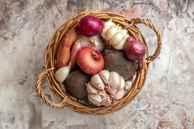 Cesta de la vista superior con verduras, ajos, cebollas y remolacha en ensalada madura de color claro.