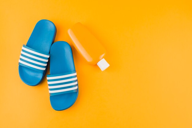 Chanclas azules con botella de loción de protección solar sobre fondo amarillo