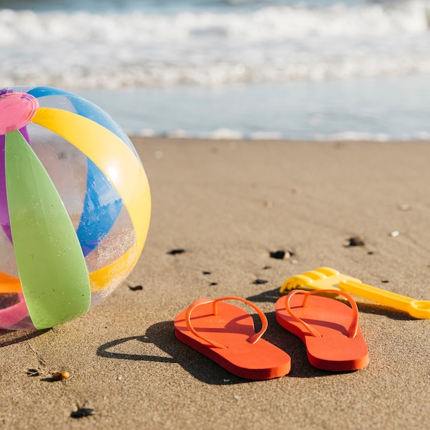 Foto gratuita chanclas y pelota inflable en la arena en la playa