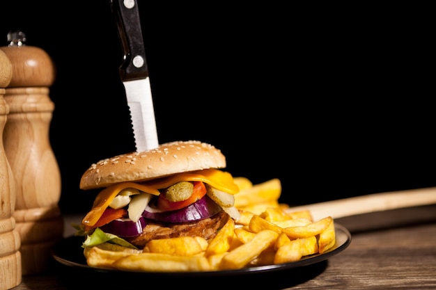 Cheesburgers caseros clásicos sobre placa negra y fondo junto a papas fritas. Comida rápida. Refrigerio poco saludable