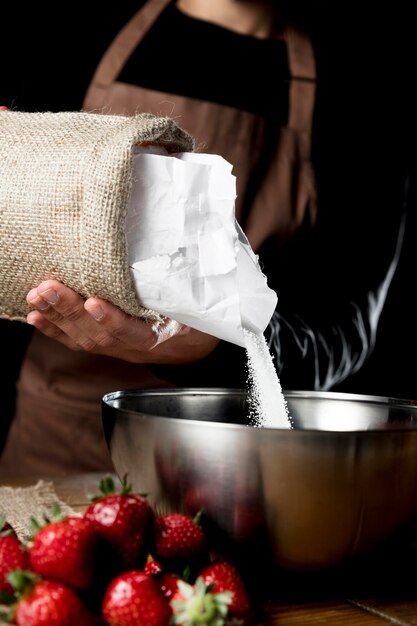 Chef agregando azúcar al tazón con fresas