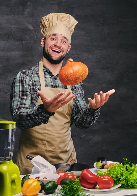 El chef barbudo sostiene calabaza cerca de la mesa con muchas verduras.