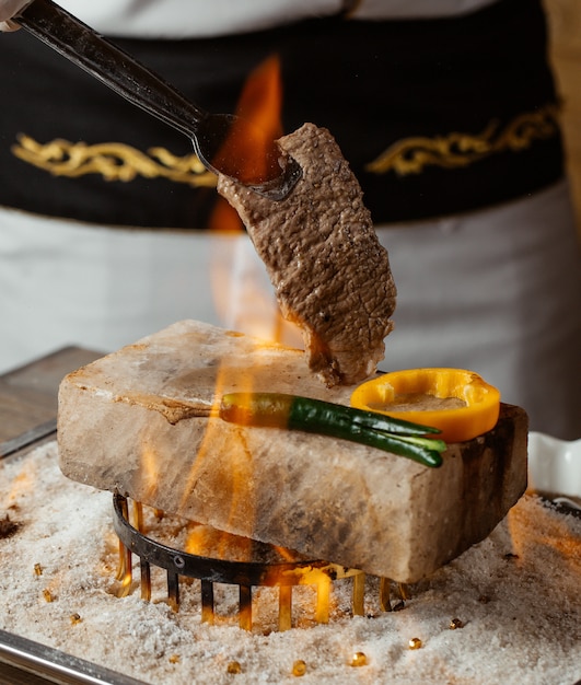 Chef con bistec en piedra con pimientos a la parrilla en llamas