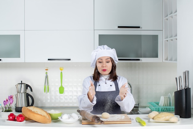 Chef de comis femenino en uniforme de pie detrás de la mesa manchando su rostro con harina en la cocina blanca