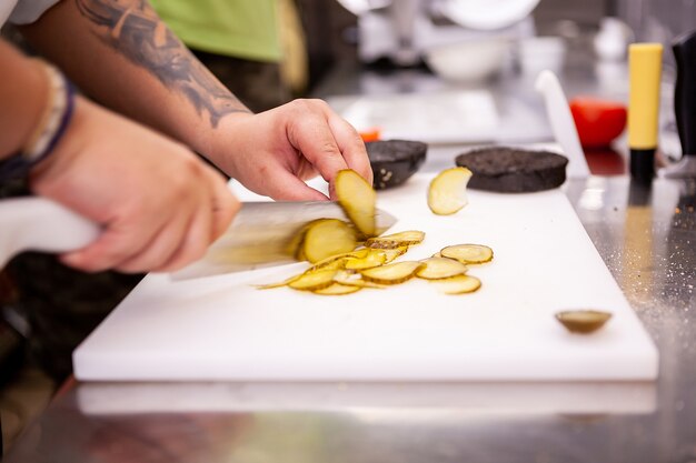 El chef corta encurtidos para una deliciosa hamburguesa en el restaurante. Preparación de comida