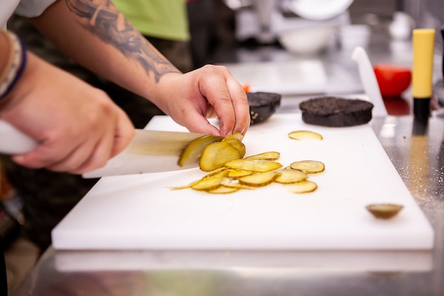 El chef corta encurtidos para una deliciosa hamburguesa en el restaurante. Preparación de comida