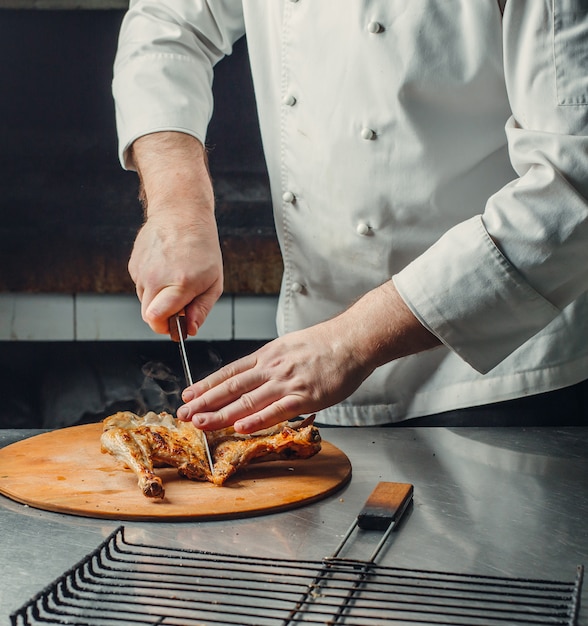 Chef cortando pollo a la parrilla sobre tabla de madera en la cocina del restaurante