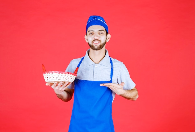 Chef en delantal azul sosteniendo una canasta de pan cubierta con una toalla roja.