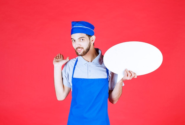 Chef en delantal azul sosteniendo un tablero de información ovale.