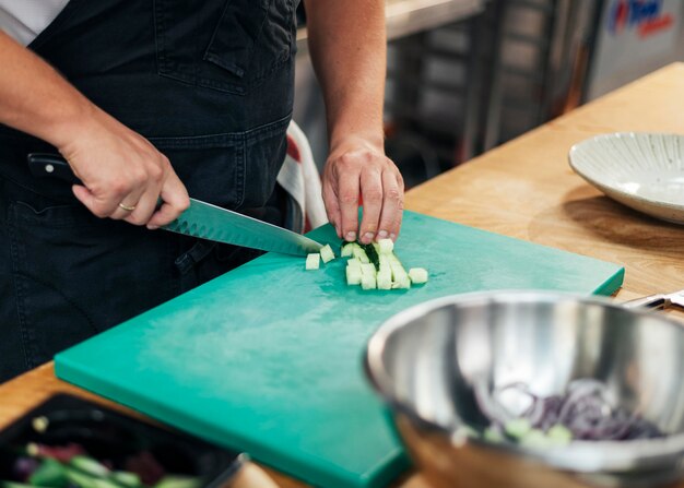 Chef con delantal para picar pepino en la cocina