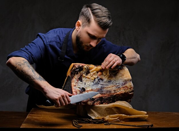 Chef enfocado cortando carne seca exclusiva en una mesa en una casa de caza sobre un fondo oscuro.