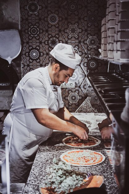 El chef experimentado está agregando decoración a la pizza recién preparada.