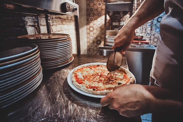 El chef experimentado está cortando pizza recién preparada con un cuchillo especial.