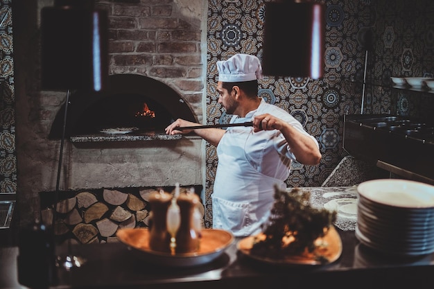 El chef experimentado está poniendo su pizza al horno con una espátula gigante especial.