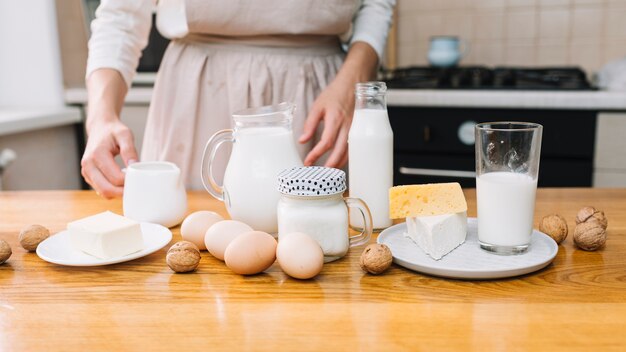 Chef femenina con queso; huevos; Nogal y leche en mesa de madera para preparar pastel.