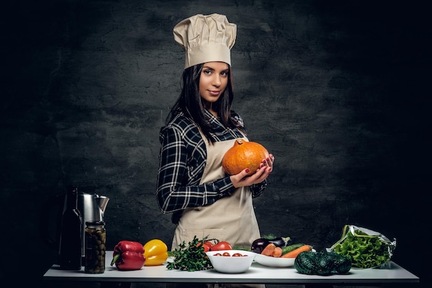 Foto gratuita la chef femenina sostiene el bombeo sobre un fondo oscuro.