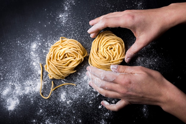 Chef haciendo tagliatelle nido de pasta con harina en polvo en la mesa de la cocina