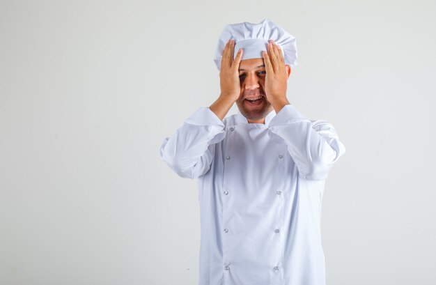 Chef hombre cogidos de la mano a la cabeza y sonriendo con sombrero y uniforme y mirando avergonzado