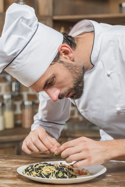 Chef hombre guarnición de fideos en el mostrador de la cocina