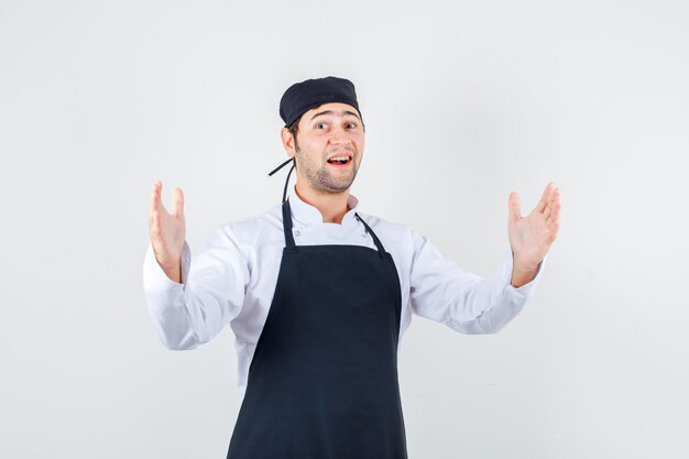 Chef hombre en uniforme, delantal levantando las manos y mirando asombrado, vista frontal.