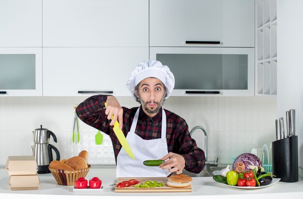 Chef hombre vista frontal sosteniendo pepino y cuchillo en la cocina