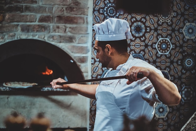 Foto gratuita el chef italiano está poniendo pizza gourmet recién hecha en el horno de piedra.