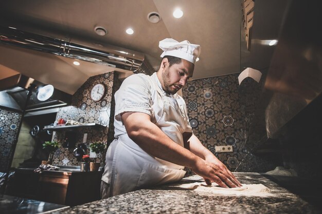 Chef italiano en uniforme está preparando pasteles para pizza en la cocina.