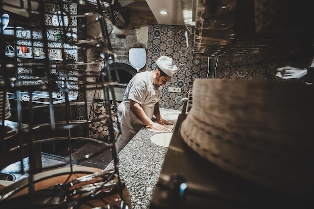 Chef italiano en uniforme está preparando pasteles para pizza en la cocina.