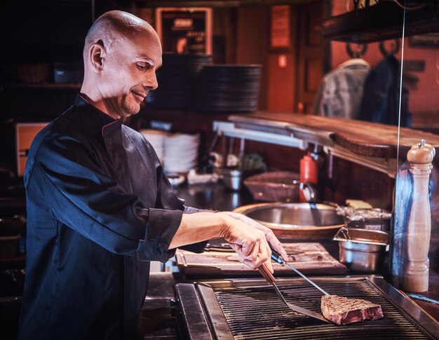 Chef maestro enfocado usando uniforme cocinando un delicioso filete de ternera en una cocina en un restaurante.