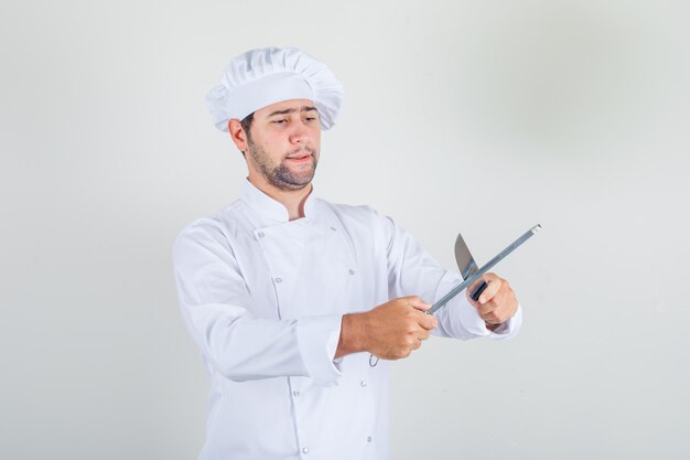 Chef masculino afilado cuchillo en uniforme blanco y mirando ocupado
