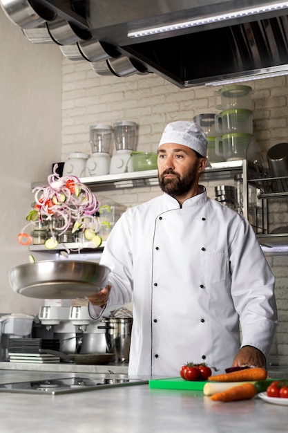 Foto gratuita chef masculino en la cocina cocinando un plato en una sartén