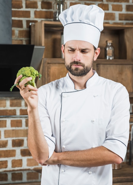 Chef masculino contemplado sosteniendo brócoli orgánico verde en su mano