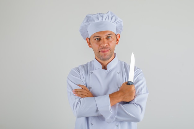 Chef masculino con cuchillo con los brazos cruzados en uniforme y sombrero y mirando confiado