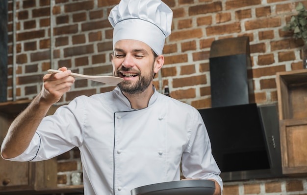 Foto gratuita chef masculino degustación de alimentos en una espátula de madera