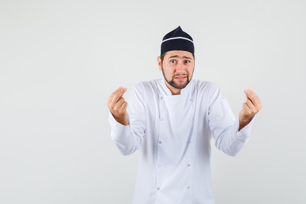 Chef masculino explicando algo en uniforme blanco y mirando indefenso, vista frontal.