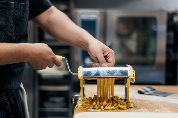 Foto gratuita chef masculino con máquina para picar masa de pasta fresca