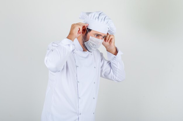 Chef masculino con máscara médica en uniforme blanco y mirando con cuidado