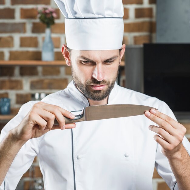 Chef masculino mirando el cuchillo filoso