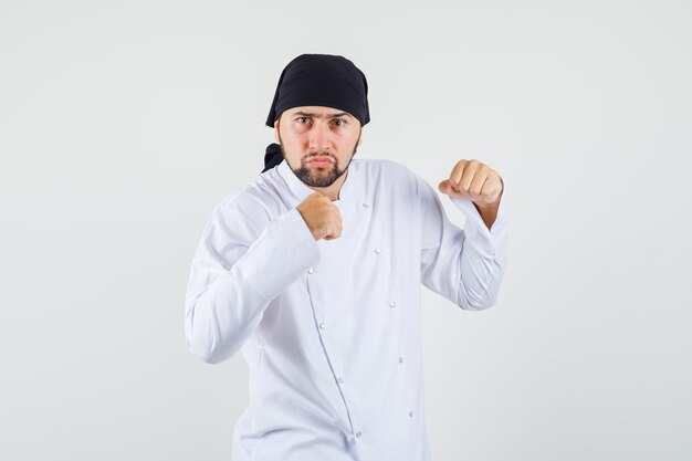 Chef masculino de pie en pose de boxeador en uniforme blanco y mirando nervioso. vista frontal.