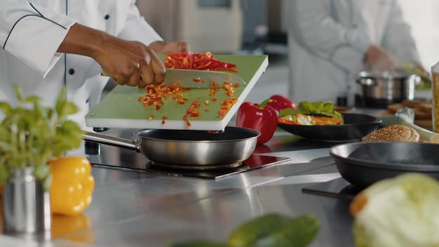 Chef masculino preparando pimiento picado en la cocina del restaurante, cocinando un plato gourmet con ingredientes frescos. Auténtico cocinero preparando comida de verduras con receta de comida culinaria. De cerca.