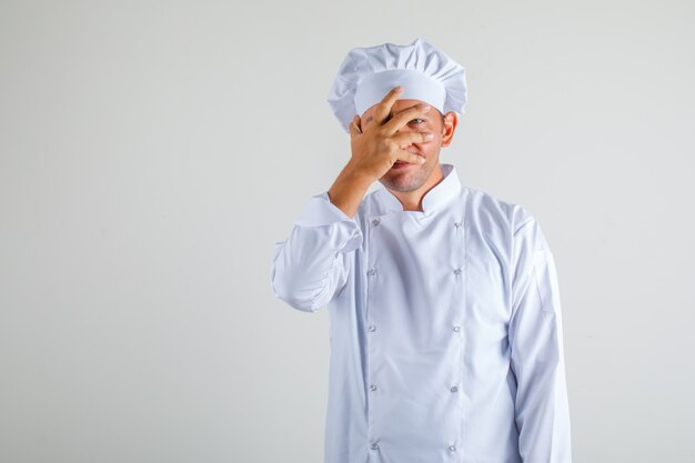 Chef masculino que cubre un ojo con la mano en el sombrero y uniforme