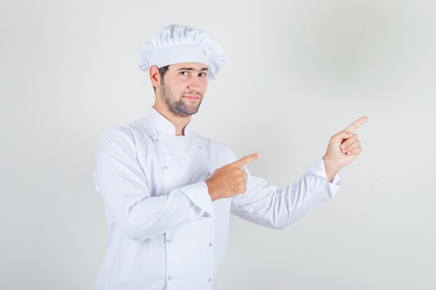 Chef masculino señalando con el dedo en uniforme blanco y mirando positivo