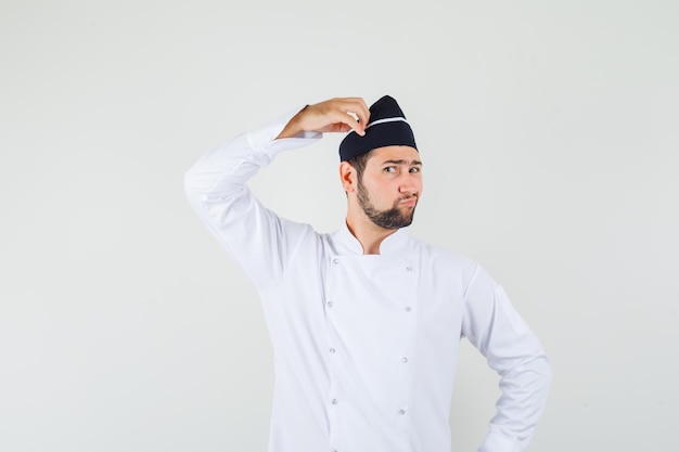 Chef masculino tocando su cabeza en uniforme blanco y mirando pensativo, vista frontal.