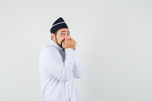 Chef masculino en uniforme blanco combinando puños en la boca y mirando emocionado, vista frontal.